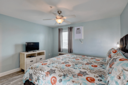 light blue motel room with single bed and TV on a stand with a window
