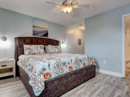 light blue painted motel room with large bed, lamps on each side, and an ocean painting above
